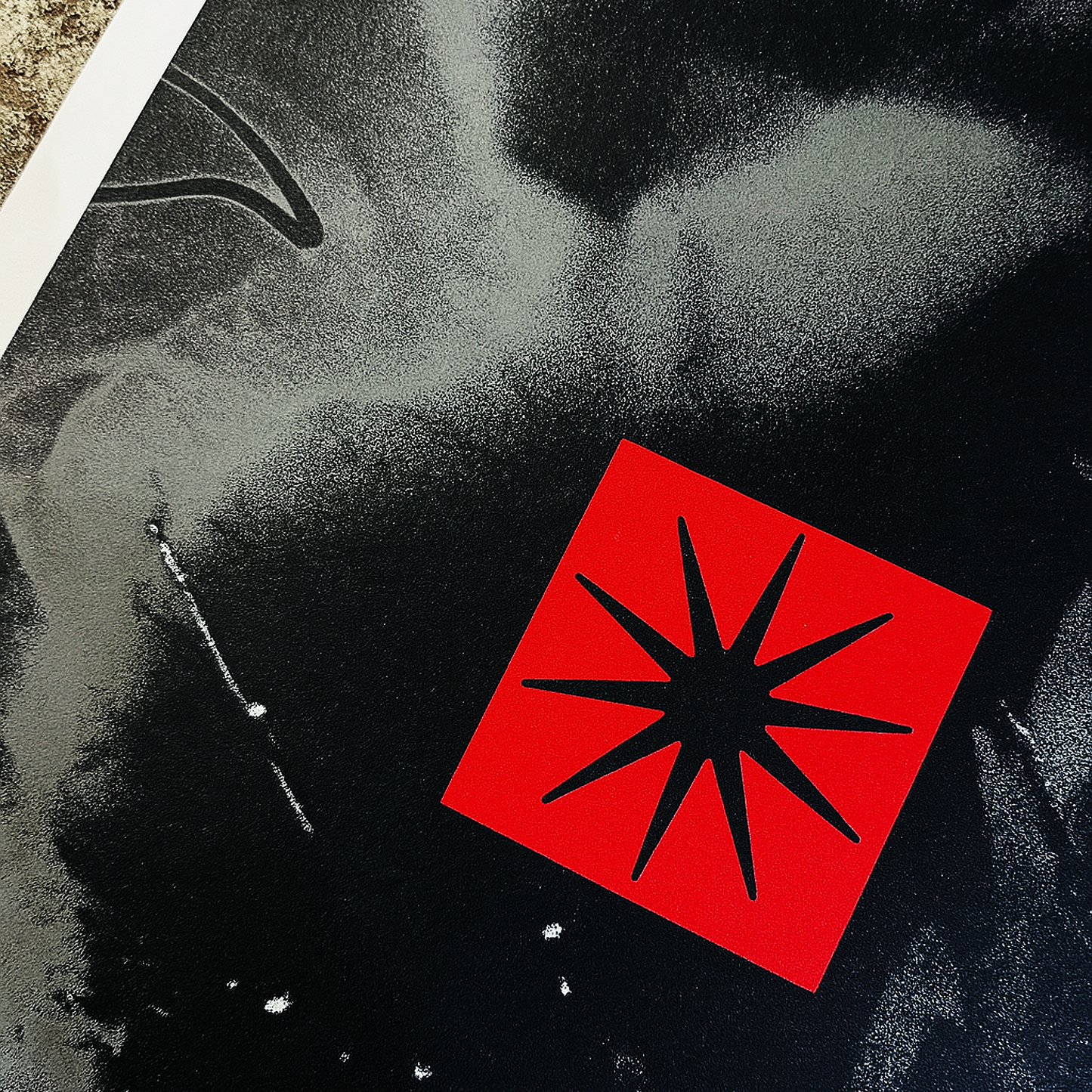 Red square with black star-like design on a textured black and gray background