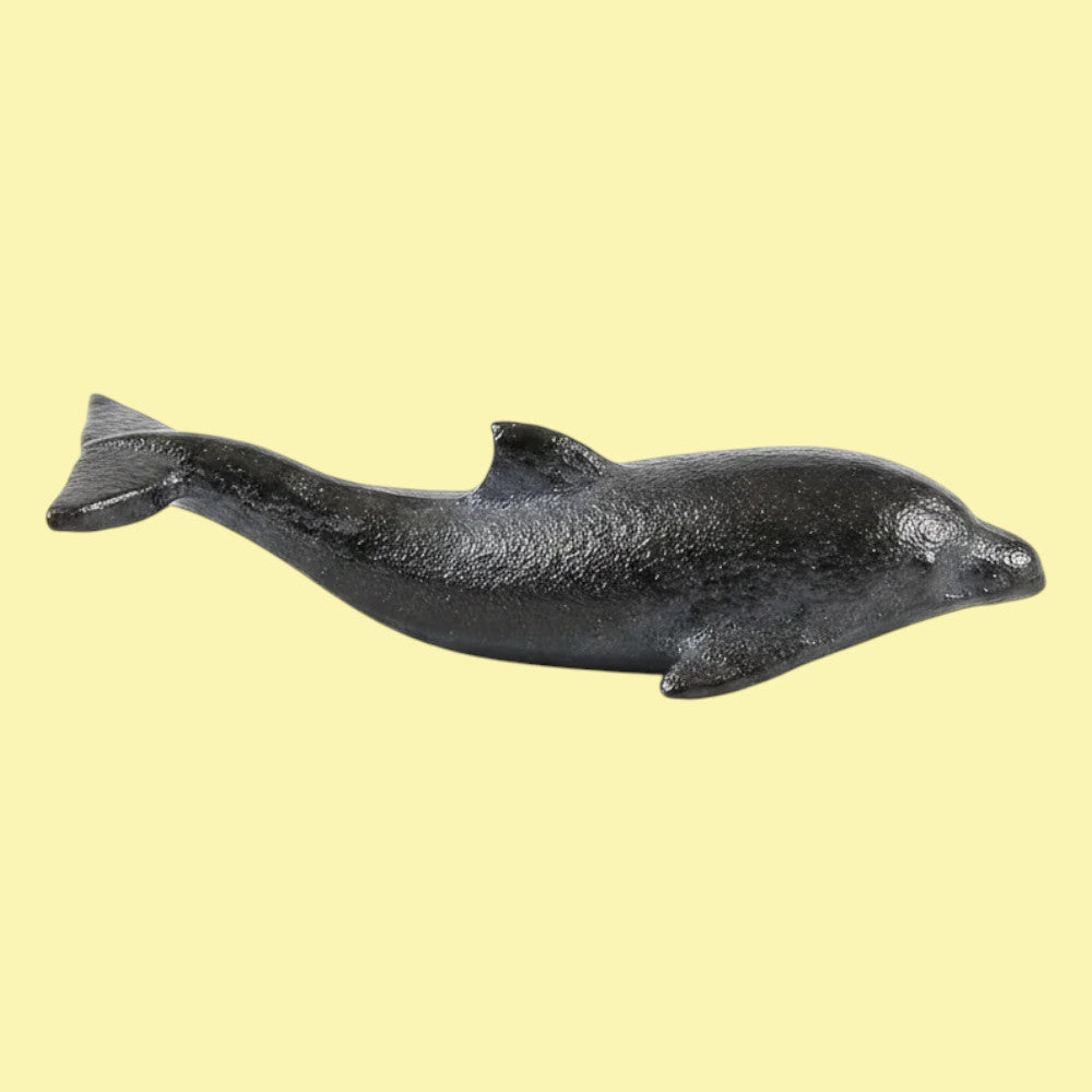 A small black cast-iron dolphin figurine shown against a solid pale yellow background.